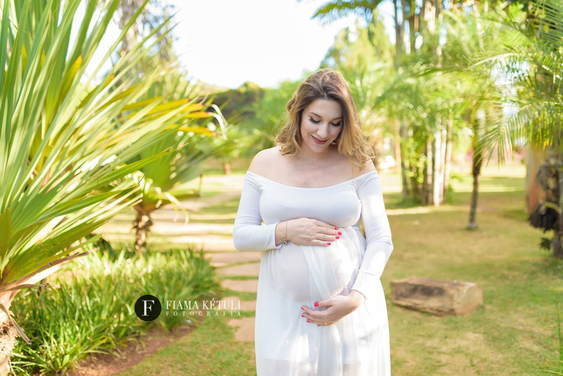 Grávida em ensaio fotográfico ao ar livre com vestido branco